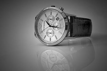 Elegant black and white close-up of a luxury wristwatch with a reflective stainless steel body and leather strap. HD wallpaper
