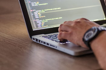 A close-up shot of a person coding on a laptop, focusing on the hands and screen. HD wallpaper