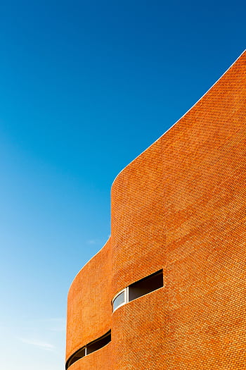 Curved brick building facade against a vibrant blue sky. HD phone wallpaper