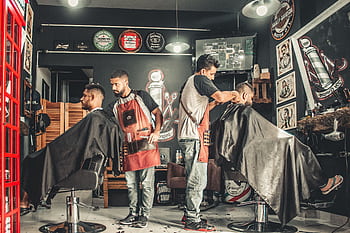 A bustling barbershop with two men getting haircuts, showcasing a vibrant barber environment. HD wallpaper