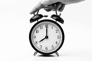A classic black and white alarm clock being held by a hand, depicting the concept of time. HD wallpaper