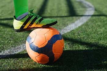 Dynamic shot of a soccer player's foot on a vivid orange ball on a lush green field. HD wallpaper