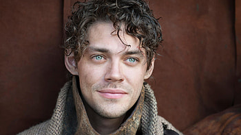 Curly Hair Blue Eyes Tom Payne Is Wearing Grey Color Dress Standing In Brown Background Boys HD wallpaper