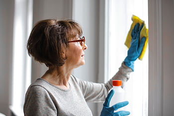 Elderly woman cleansing window indoors using gloves and cleaner. HD wallpaper