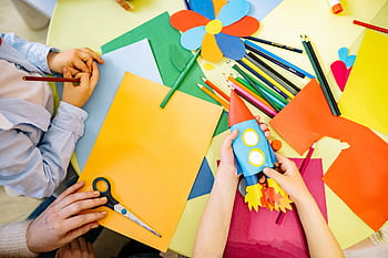 Children engaged in a vibrant arts and crafts session with paper and pencils. Perfect for education and creativity themes. HD wallpaper