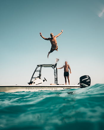 Two men enjoy a sunny adventure, jumping into the Abu Dhabi sea from a boat. HD phone wallpaper
