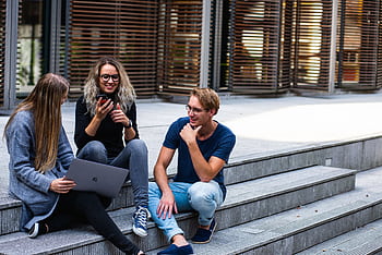 Three young professionals having a friendly chat while sitting on outdoor steps. HD wallpaper