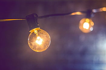 Close-up of an illuminated vintage-style string light bulb on a dark background. HD wallpaper