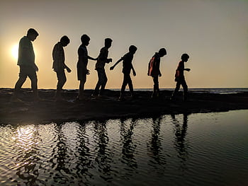 A group of children walk along the shoreline, silhouetted against a sunset, reflecting in the water. HD wallpaper