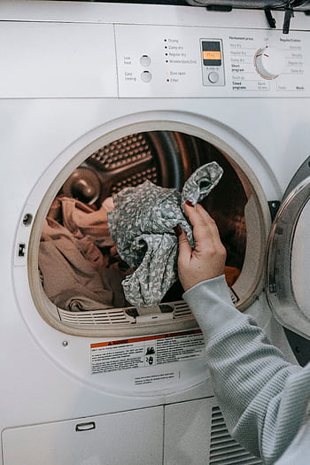 Close-up of a woman loading clothes into a washing machine, highlighting domestic chores and daily routine. HD phone wallpaper