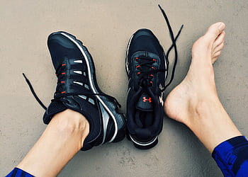 A pair of black sneakers next to bare feet on a gray surface. HD wallpaper