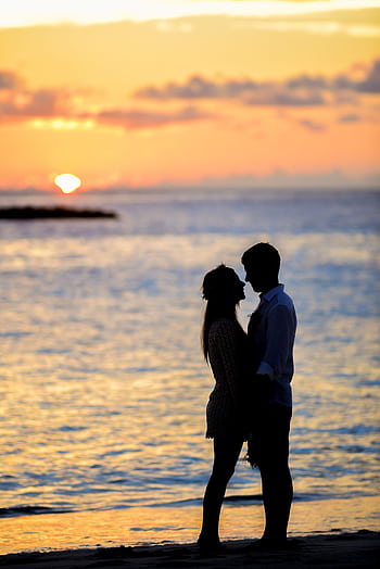 A couple sharing a romantic moment on a beach at sunset, creating a beautiful silhouette. HD phone wallpaper
