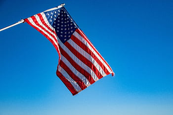The American flag proudly waves on a flagpole against a clear blue sky, symbolizing dom and patriotism. HD wallpaper