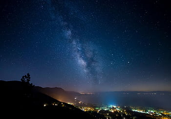 Captivating view of the Milky Way galaxy over the serene Lake Tahoe with twinkling city lights. HD wallpaper