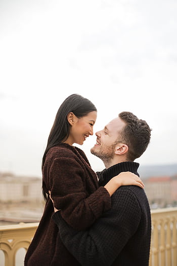Smiling couple embracing lovingly on a bridge outdoors, exuding romance and joy. HD phone wallpaper