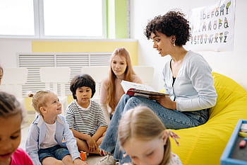 Teacher reading to preschool kids in a colorful classroom setting. HD wallpaper