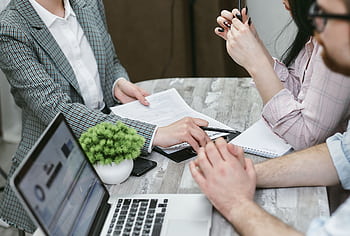 Professional meeting discussing business agreements with laptops and documents on a rustic table. HD wallpaper