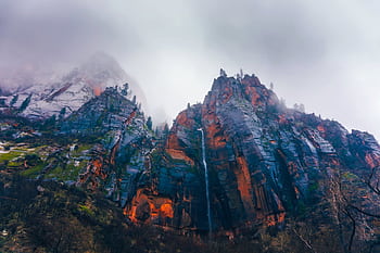 A stunning mountain peak enveloped in fog features a cascading waterfall. HD wallpaper