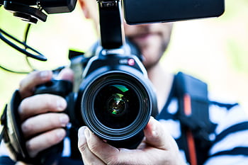A close-up shot of a cameraman filming, focusing on the camera lens and equipment. HD wallpaper