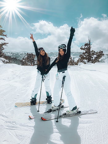 Two women posing on a snowy slope, enjoying a bright winter day of skiing and snowboarding. HD phone wallpaper