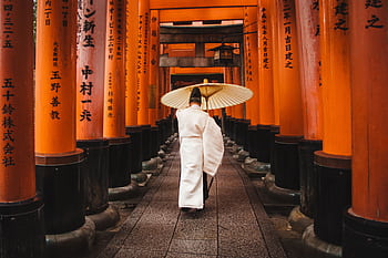 A person in traditional attire walks through the iconic torii gates at Fushimi Inari Shrine, Kyoto. HD wallpaper