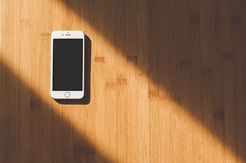 A sleek white smart lies on a sunlit wooden table, creating a minimalist tech aesthetic. HD wallpaper