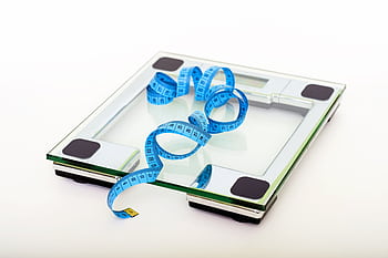 A digital glass weighing scale with a blue measuring tape, symbolizing weight management. HD wallpaper