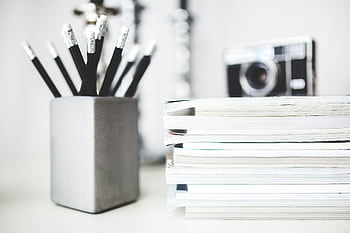Organized workspace featuring pencils in holder and stacked magazines with a vintage camera in the background. HD wallpaper