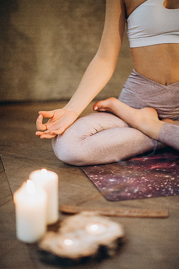 A woman practicing yoga indoors in lotus pose with candles creating a calming atmosphere. HD phone wallpaper