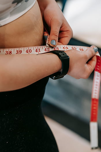 Woman measuring her waist with a tape measure, focusing on fitness and weight management. HD phone wallpaper