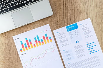 Top view of a laptop, charts, and resume on a wooden desk, showcasing business analysis and job application. HD wallpaper