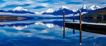 A serene lake with snowcapped mountains reflecting in the water, enhancing the tranquil outdoor setting. HD wallpaper