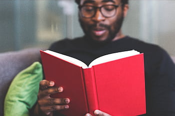 Focused young man reading a red book indoors, showcasing learning and relaxation. HD wallpaper