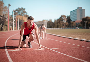 Male athlete in starting position on outdoor track with blurred background. HD wallpaper