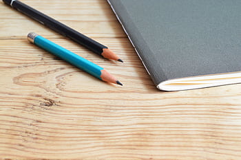 A minimalist composition of a notebook and pencils on a wooden desk, ideal for study themes. HD wallpaper