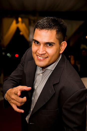 Portrait of a confident, smiling businessman in a formal suit pointing directly at the camera indoors. HD phone wallpaper