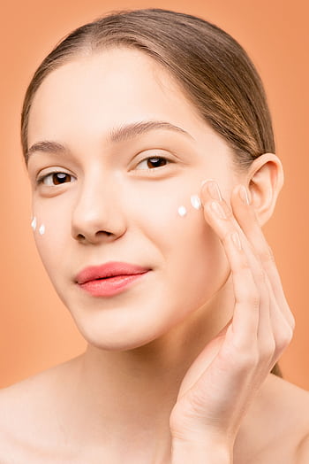 Young woman applying facial cream for healthy skincare routine. HD phone wallpaper