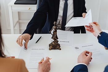 Three adults discussing divorce documents in a formal office setting with legal statue in view. HD wallpaper