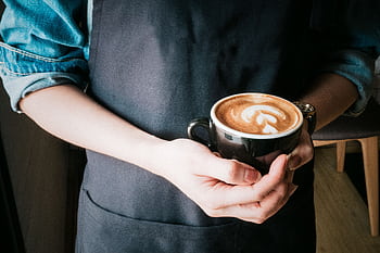 A barista holds a coffee cup with beautiful latte art in a cozy café setting. HD wallpaper