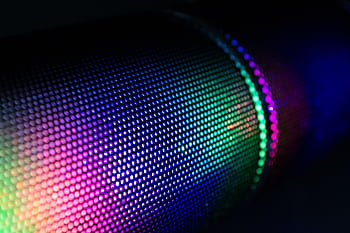 Close-up of a wireless speaker with colorful RGB lighting illuminating the mesh surface. HD wallpaper