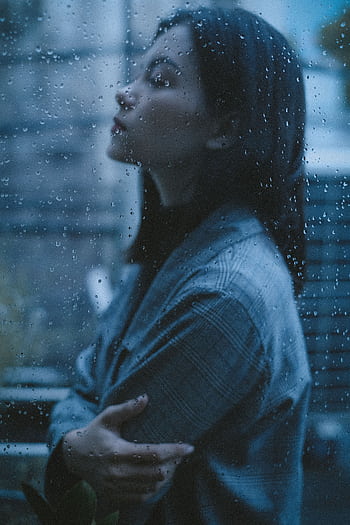 Side profile of a woman in contemplation through a rain-soaked window, embodying solitude and reflection. HD phone wallpaper