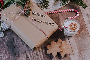 Celebrate Christmas with a wrapped gift, cookies, and festive drink on a cozy wooden table. HD wallpaper