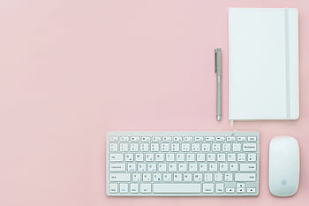 Flat lay of a minimalist workspace featuring a keyboard, notebook, and pen on a pink surface. HD wallpaper
