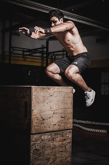 Shirtless man showcasing strength and fitness with a box jump in an indoor gym setting. HD phone wallpaper