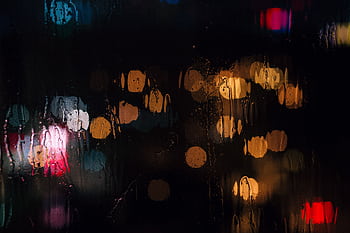 Blurry colorful bokeh lights on a wet window at night create an artistic and moody ambiance. HD wallpaper