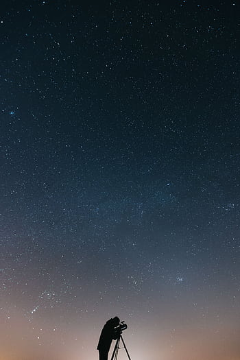 A lone astronomer using a telescope to observe the vast, starry night sky. HD phone wallpaper