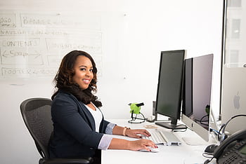 Confident businesswoman seated at her desk in an office, typing on a computer. HD wallpaper