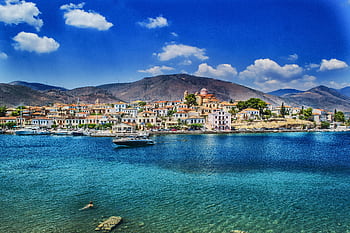 Beautiful coastal view of a charming Greek town against a mountainous backdrop, ideal for travel and vacation ry. HD wallpaper