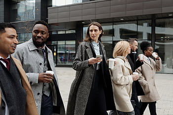 A diverse group of business professionals walking outside a modern building, enjoying coffee and conversation. HD wallpaper