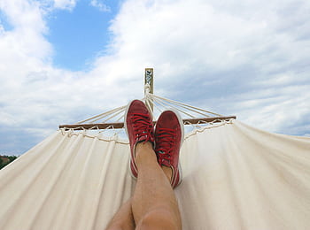 Feet resting on a hammock with red sneakers, epitomizing summer relaxation and leisure outdoors. HD wallpaper